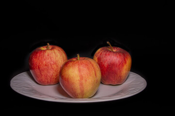 ceramic plate with three red apples isolated on black background