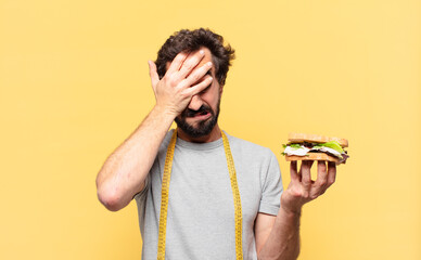 young crazy bearded man dieting sad expression and holding a sandwich