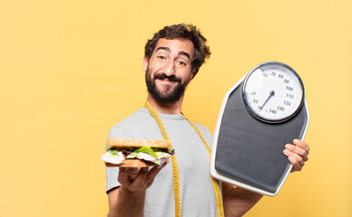 young crazy bearded man dieting happy expression and holding a weight scale and a sandwich