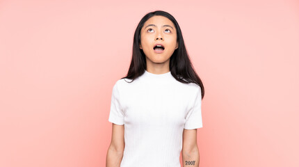 Teenager Chinese woman isolated on pink background looking up and with surprised expression