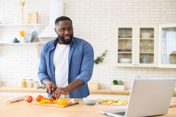 Focused handsome African American guy watching cooking classes and learning how to make delicious...