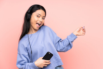 Naklejka premium Teenager Chinese girl isolated on pink background listening music and doing guitar gesture