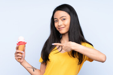 Teenager Asian girl with a cornet ice cream isolated on blue background and pointing it