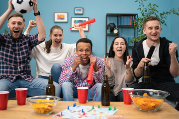 Very excited friends having fun by watching football match and eating at home, indoors. Friendship, leasure, rest, home party concept