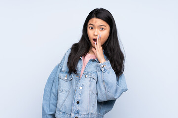 Teenager Chinese woman isolated on blue background whispering something with surprise gesture while looking to the side