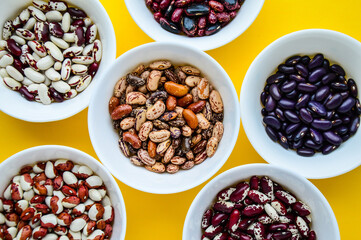 Different varieties of beans in white masks isolated on a yellow background. Multicolored mixed beans. Seeds.