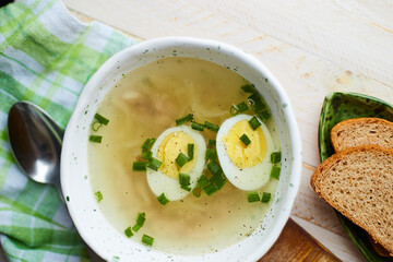 Handmade ceramic bowl with chicken soup, boiled eggs and fresh green onion on a table.