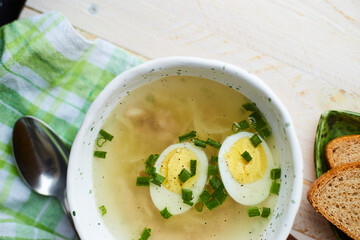 Handmade ceramic bowl with chicken soup, boiled eggs and fresh green onion on a table.