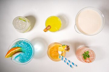 Colorful summer drinks set. Various bright alcohol cocktails and beverages, in different glasses, with tropical fruit on white background copy space