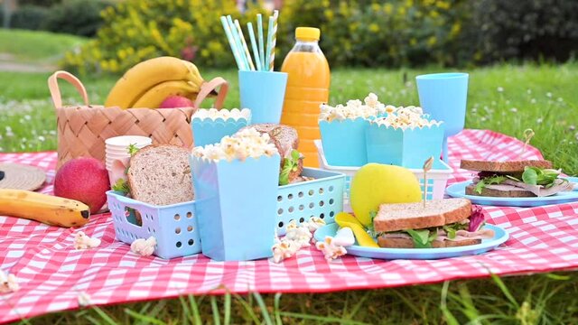 Lunch in the park on the green grass. Summer sunny day and picnic basket. Popcorn and sandwiches for a snack outdoors in nature. in bright plastic dishes on a checkered tableclot. ootage, Slow motion