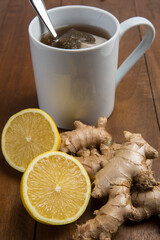 Cup of lemon ginger tea with raw ginger and lemon isolated on wood background