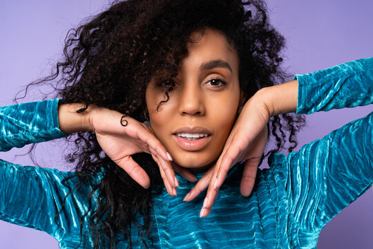 Close up  studio fashion portrait of gorgeous brazillian woman with curly hairs in elegant velvet dress over blue violet background.  hends near face.