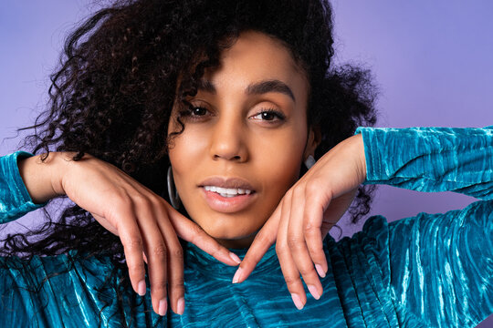Close up  studio fashion portrait of gorgeous brazillian woman with curly hairs in elegant velvet dress over blue violet background.  hends near face.