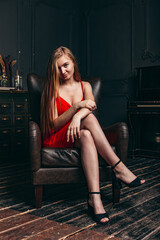 Fototapeta na wymiar beautiful girl in a red dress sits in a chair in a photo studio