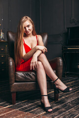 Obraz na płótnie Canvas beautiful girl in a red dress sits in a chair in a photo studio