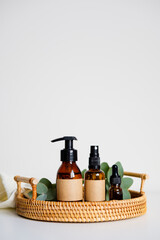Amber glass cosmetic bottles in rattan tray with eucalyptus leaves and towel. Natural organic eco beauty products.