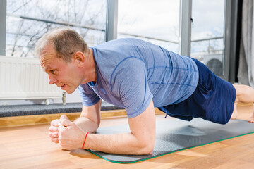Aged fit sportsman stand in plank yoga fitness pose on floor mat in room, face close up, healthy lifestyle. Close-up.