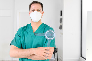 Fototapeta na wymiar Friendly male physiotherapist posing with tools in modern clinic wearing protective face mask during coronavirus pandemic. High quality photo