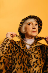 Woman wearing leopard fur coat adjusting her collar while standing at studio