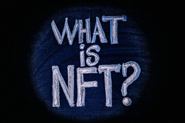 Photo on NFT (non-fungible token) theme. The question "What is NFT?", in the center of the light circle, is drawn with crayons on a chalk board