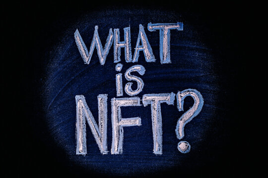 Photo on NFT (non-fungible token) theme. The question "What is NFT?", in the center of the light circle, is drawn with crayons on a chalk board