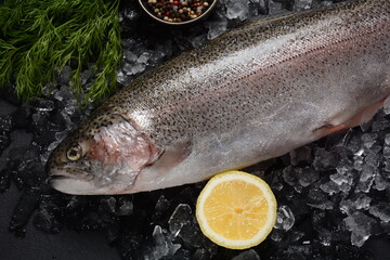 Fresh trout on dark table with lemon, pepper and dill. Tasty fish ready for cooking. Healthy seafood and dieting concept.