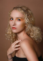 Portrait of a curly blonde girl with orange make up on brown background