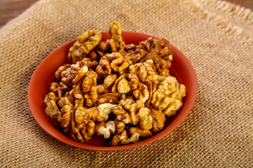 Walnuts in a clay plate on burlap on a wooden table.