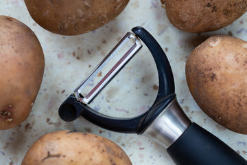 Several organic potatoes and a potato peeler on the table. Made in natural light, soft shadows.