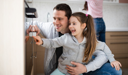 Small girl with father at home in kitchen.