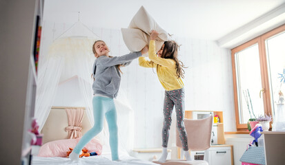Two small girls sisters indoors at home, pillow fight in bedroom.