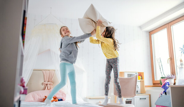 Two Small Girls Sisters Indoors At Home, Pillow Fight In Bedroom.