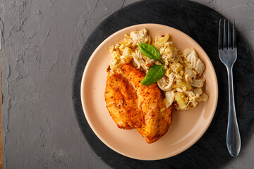 Baked chicken breast on a beige plate with pineapple salad on a table on a round stand on a concrete background next to a fork.
