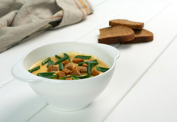 Cheese soup with croutons and green onions, slices of bread on a white wooden table.