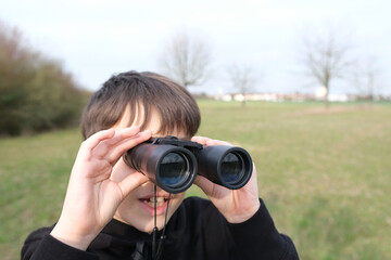 boy, guy 8-10 years old stalker looks through black binoculars in the park, spies, hunts down secrets, the concept of surveillance, observation of people and animals