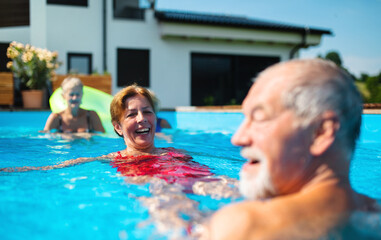 Group of cheerful seniors in swimming pool outdoors in backyard, having fun.
