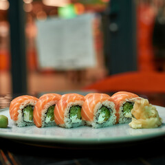 Close up shot of sushi rolls with salmon, avocado and cheese laid out on a plate on table of Japanese restaurant