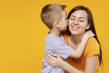 Woman have fun child baby boy 5-6-7 years old age in violet t-shirt whispering tells secret behind hand sharing news Mommy little kid son isolated on yellow background studio Mother's Day love family
