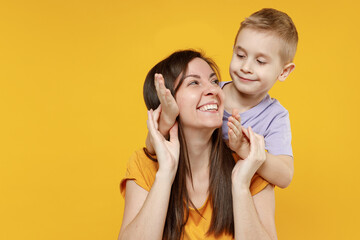 Happy young woman have fun with child baby boy 5-6-7 years old in violet tshirt Mommy little kid son close eyes with hands play guess who isolated on yellow background studio Mother's Day love family