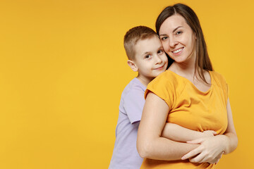 Happy young woman have fun with cute child baby boy 5-6-7 years old in violet t-shirt. Mommy little kid son posing together hugs isolated on yellow background studio. Mother's Day love family concept.
