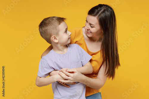 Happy young woman have fun with cute child baby boy 5-6-7 years old in violet t-shirt. Mommy little kid son posing together hugs isolated on yellow background studio. Mother's Day love family concept.