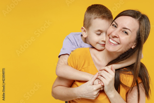 Happy young woman have fun with cute child baby boy 5-6-7 years old in violet t-shirt. Mommy little kid son posing together hugs isolated on yellow background studio. Mother's Day love family concept.
