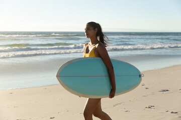 Naklejka na ściany i meble Happy mixed race woman carrying surfboard on the beach