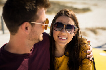 Happy caucasian couple by the sea embracing wearing sunglasses smiling