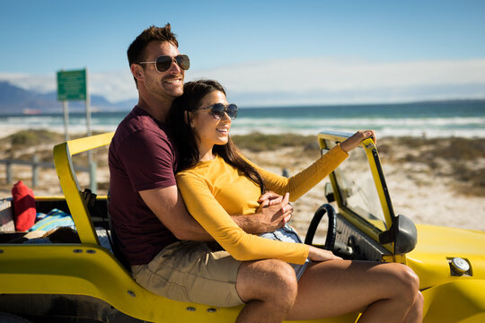 Happy caucasian couple sitting on beach buggy by the sea embracing