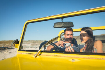 Happy caucasian couple sitting in beach buggy by the sea using smartphone