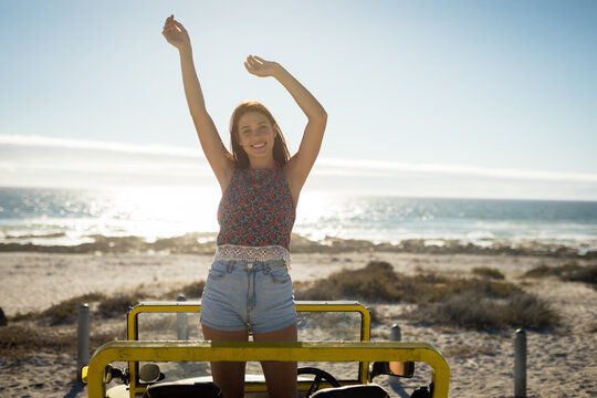 Happy caucasian woman in beach buggy by the sea with hands up looking to camera