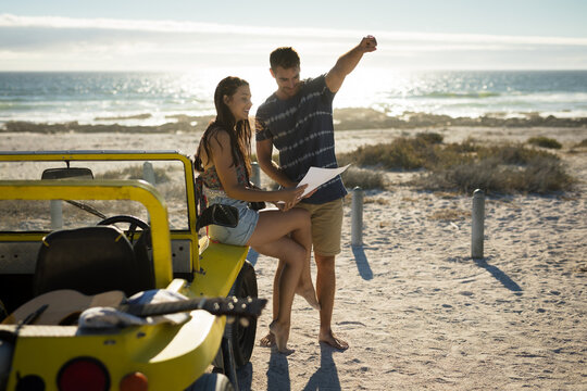 Happy caucasian couple sitting on beach buggy by the sea reading roadmap pointing - Powered by Adobe