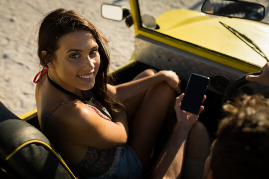 Happy caucasian couple sitting in beach buggy by the sea using smartphone - Powered by Adobe