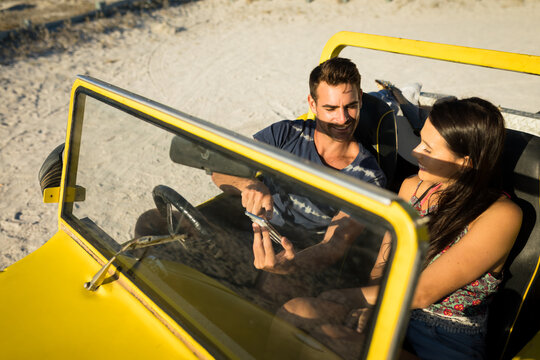 Happy caucasian couple sitting in beach buggy by the sea using smartphone - Powered by Adobe